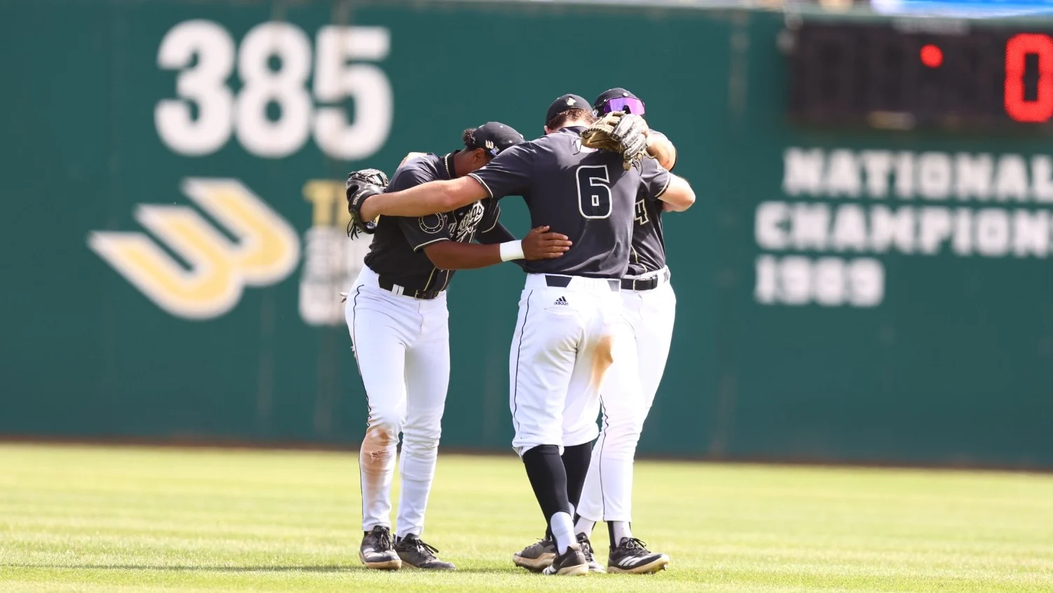 Cal Poly baseball players huddle on the field in Mustangs uniforms