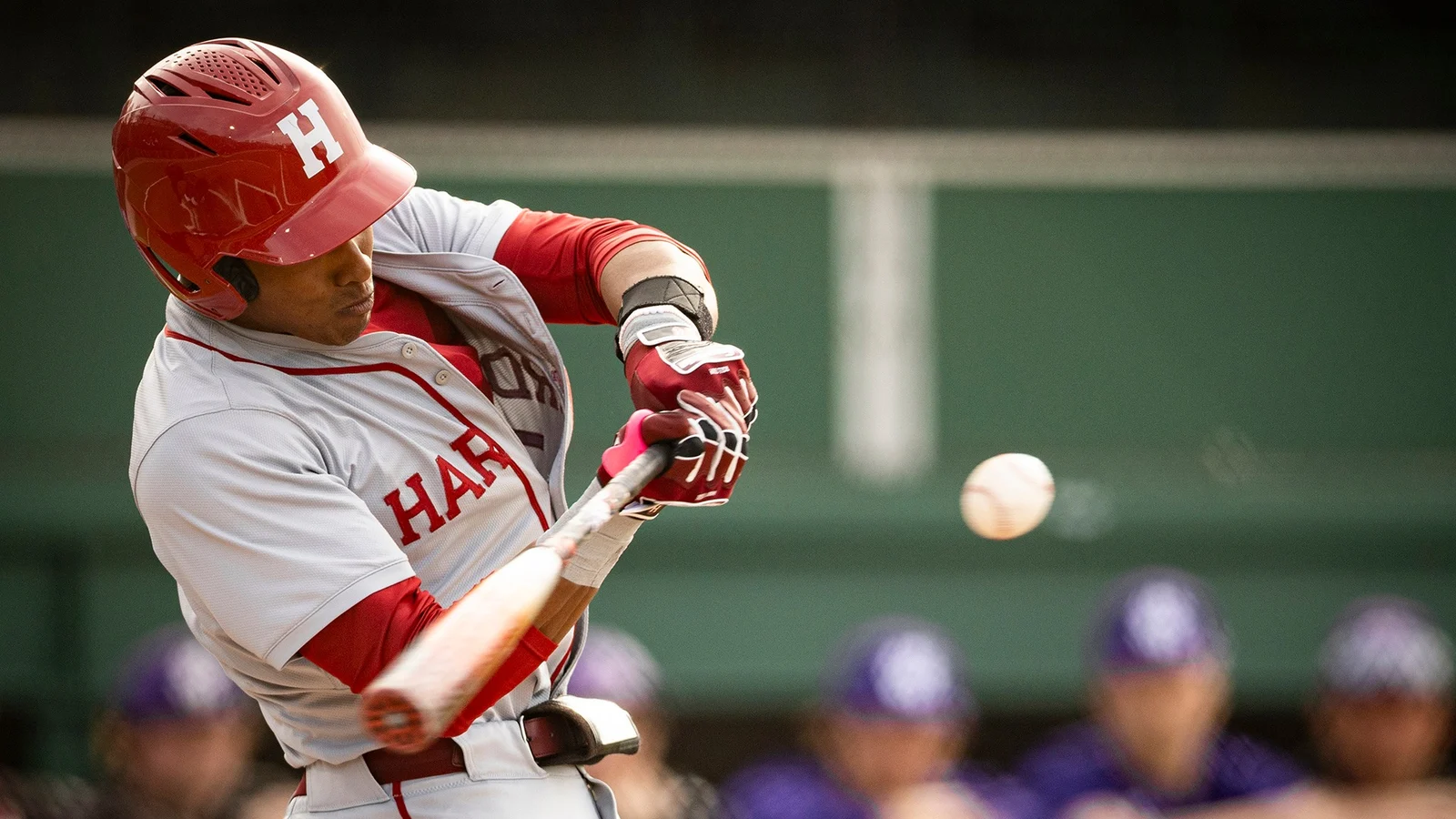 A Harvard baseball player bats in a Crimson uniform