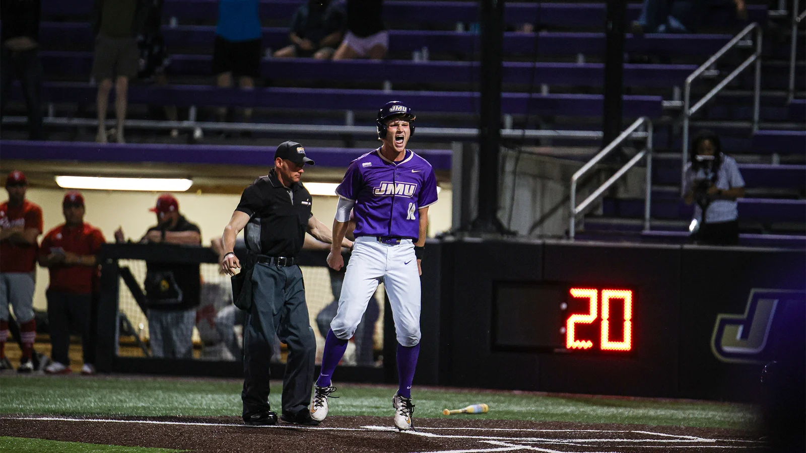 A James Madison baseball player stands at home plate in a purple Dukes uniform