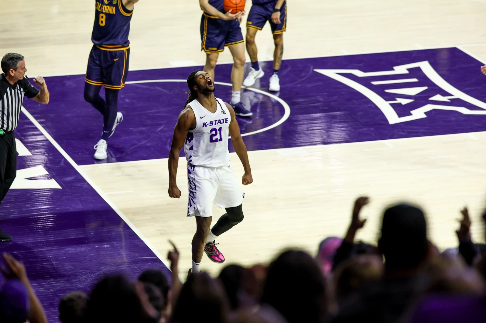 A Kansas State men's basketball player handles the ball in a white Wildcats uniform on the home court