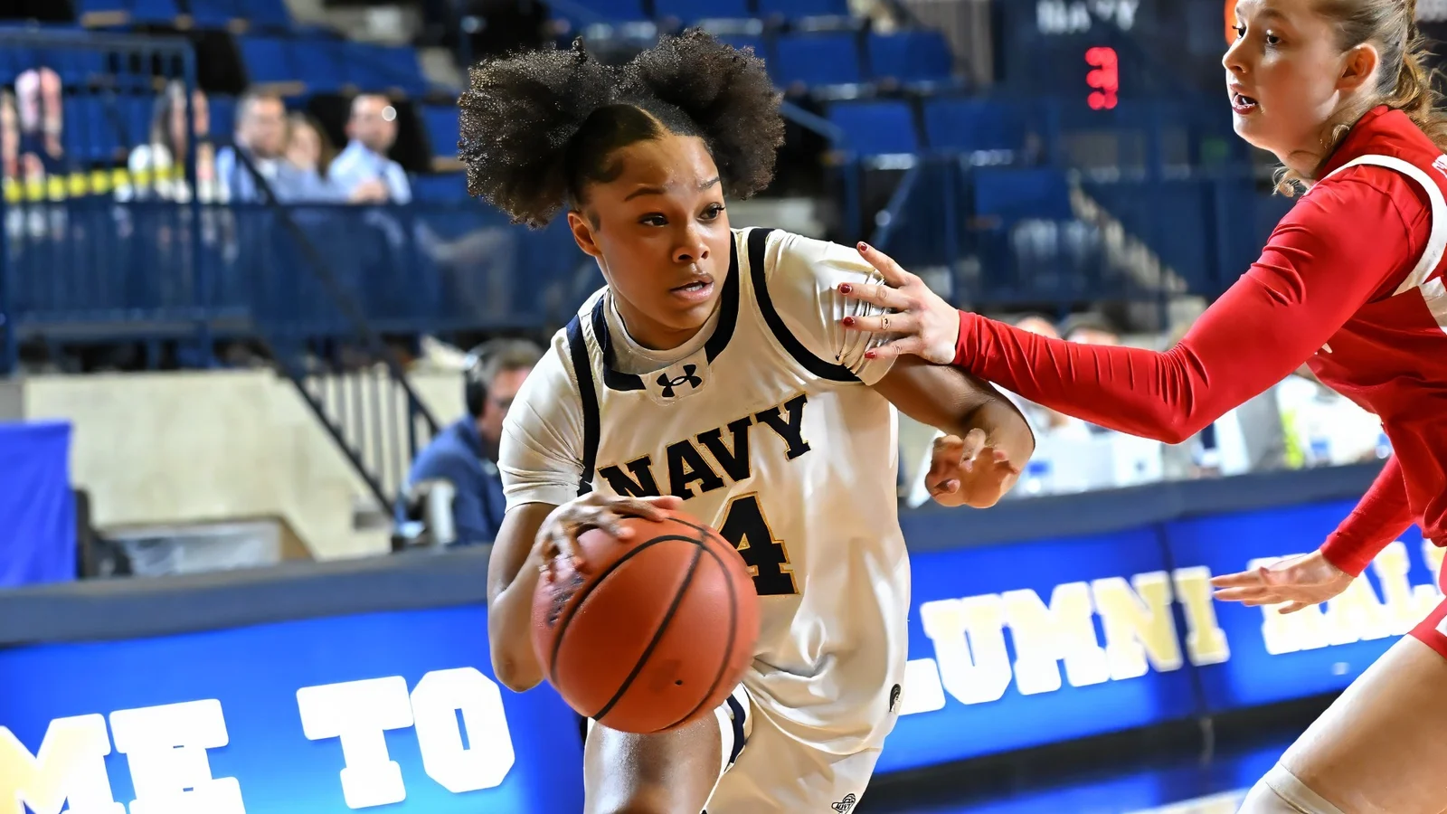 A Navy women's basketball player drives against Boston University in a white Midshipmen uniform