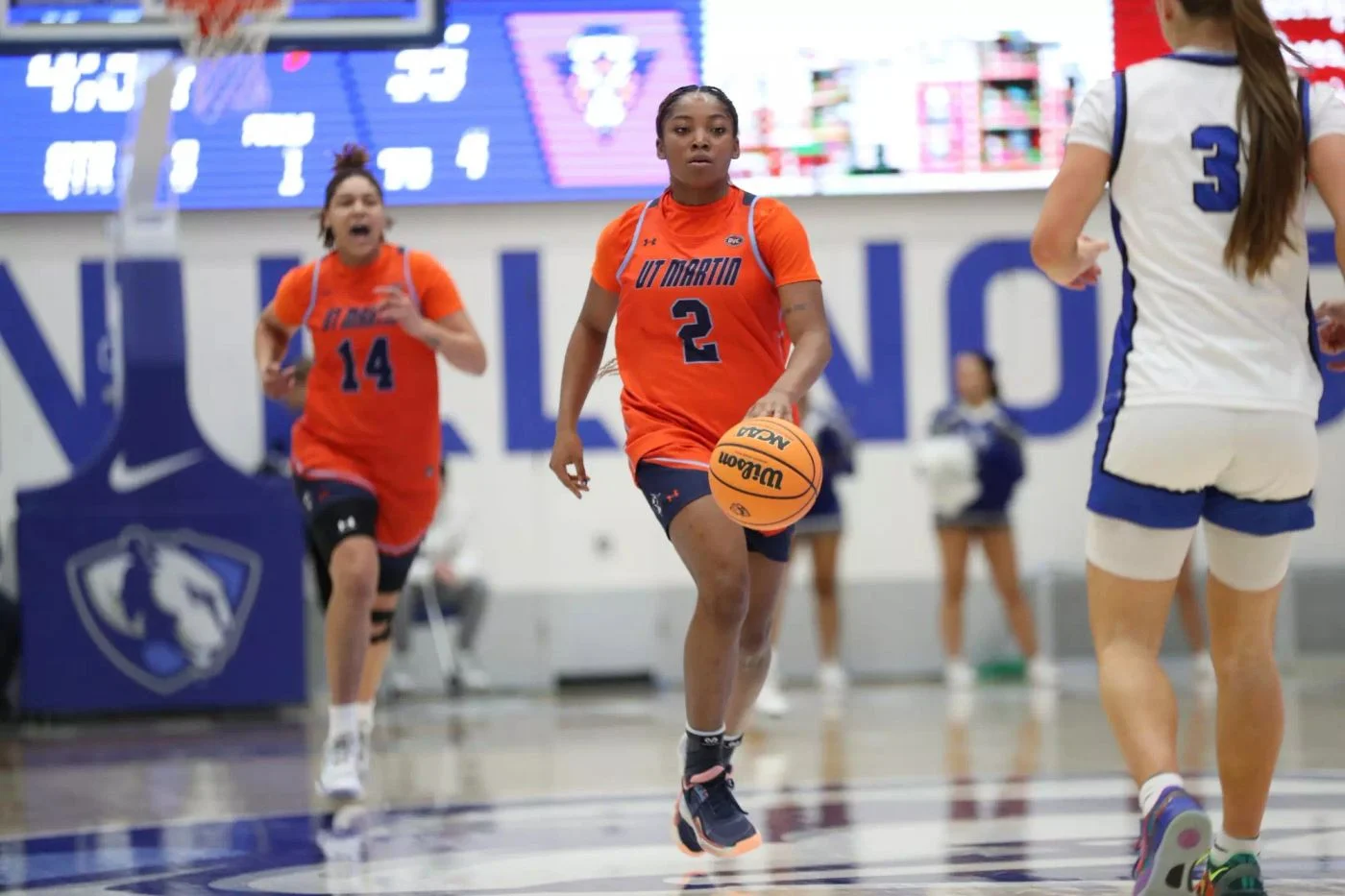 A UT Martin women's basketball player in an orange Skyhawks uniform brings the ball up court against Eastern Illinois